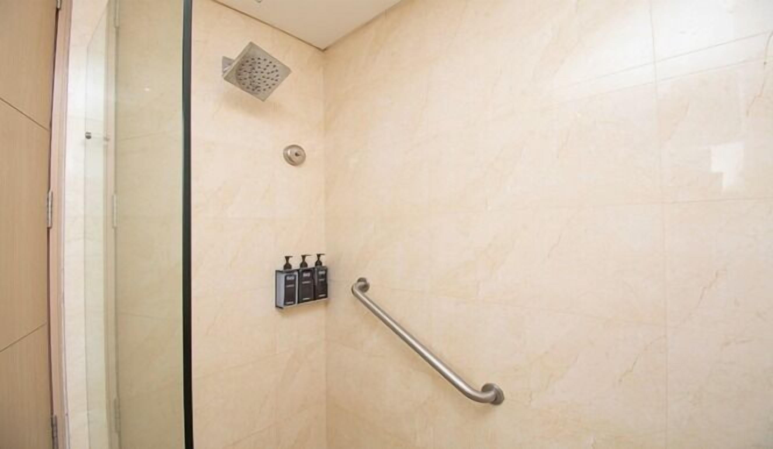 A shower with a glass door, a handheld showerhead, and a grab bar.