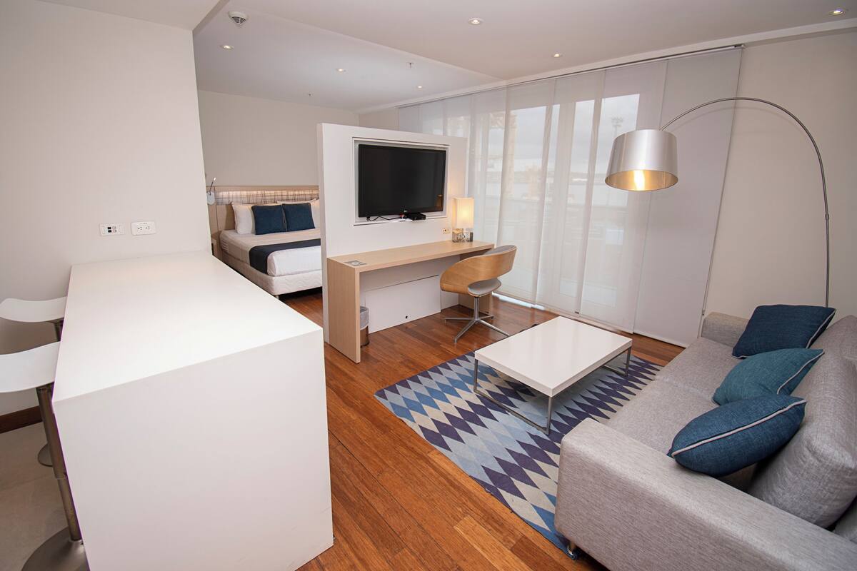 Een moderne hotelkamer met een houten vloer, een bank, een bureau met een televisie, een stoel en een lamp.