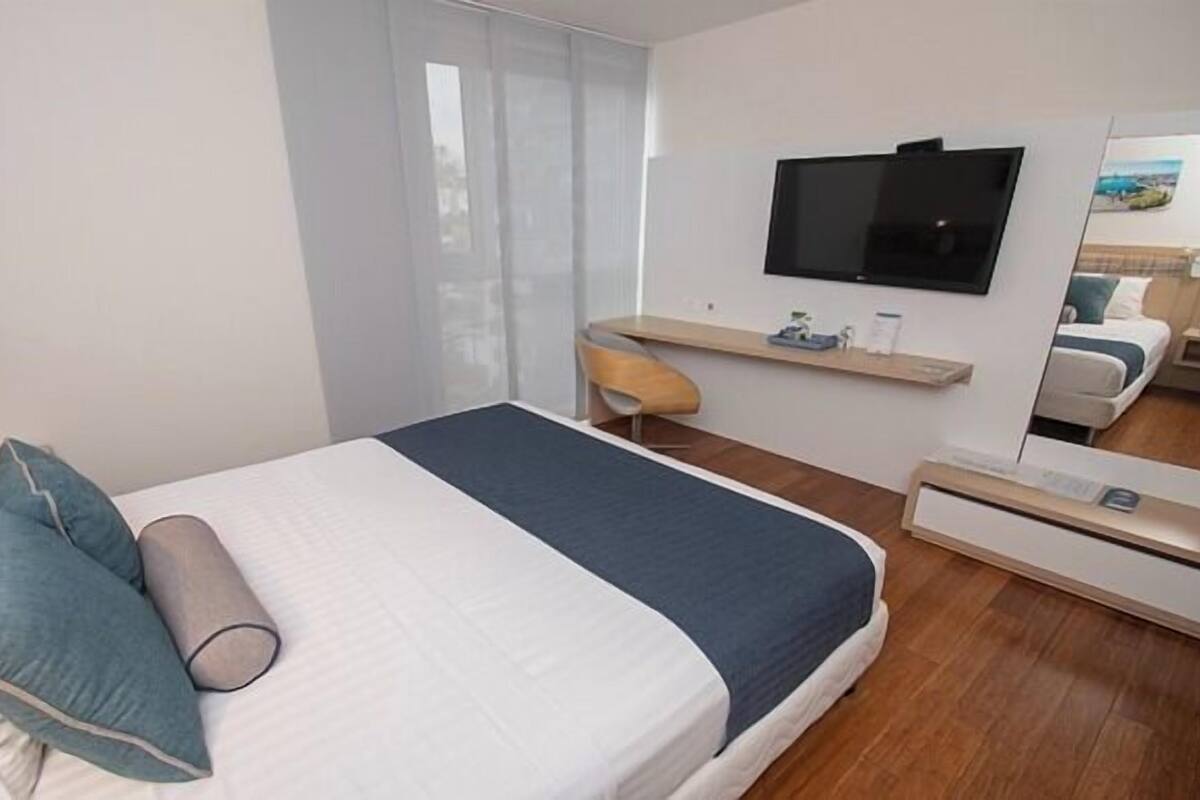 Een moderne hotelkamer met een bed, een bureau, een stoel, een televisie en een spiegel.