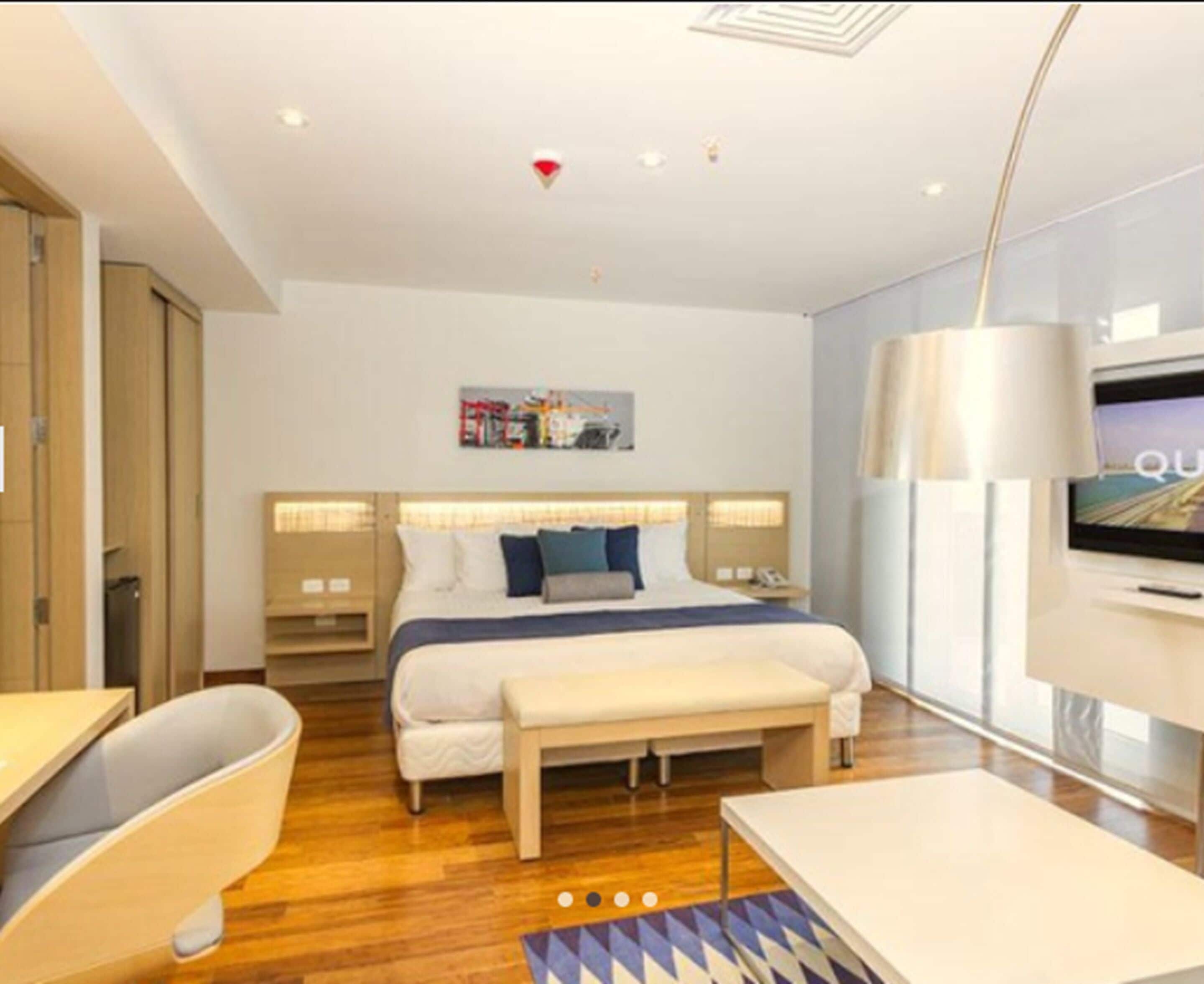 Una habitación de hotel moderna con una cama grande, mesitas de noche, un escritorio, una silla y un televisor.
