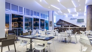 A modern restaurant with white and brown chairs, a bar area, and a large window overlooking the city. - Cosmos Pacifico Hotel (Buenaventura)