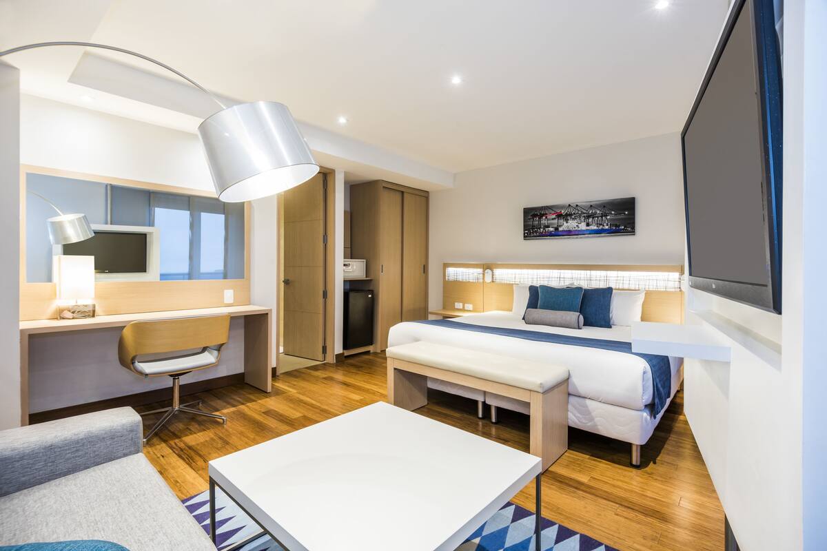 Een moderne hotelkamer met een bed, bureau, stoel en een groot raam.
