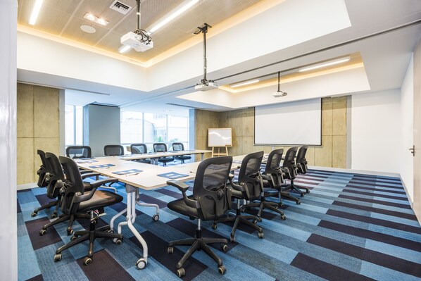 Une salle de conférence équipée d’une longue table, de plusieurs chaises, d’un projecteur et d’un tableau blanc.