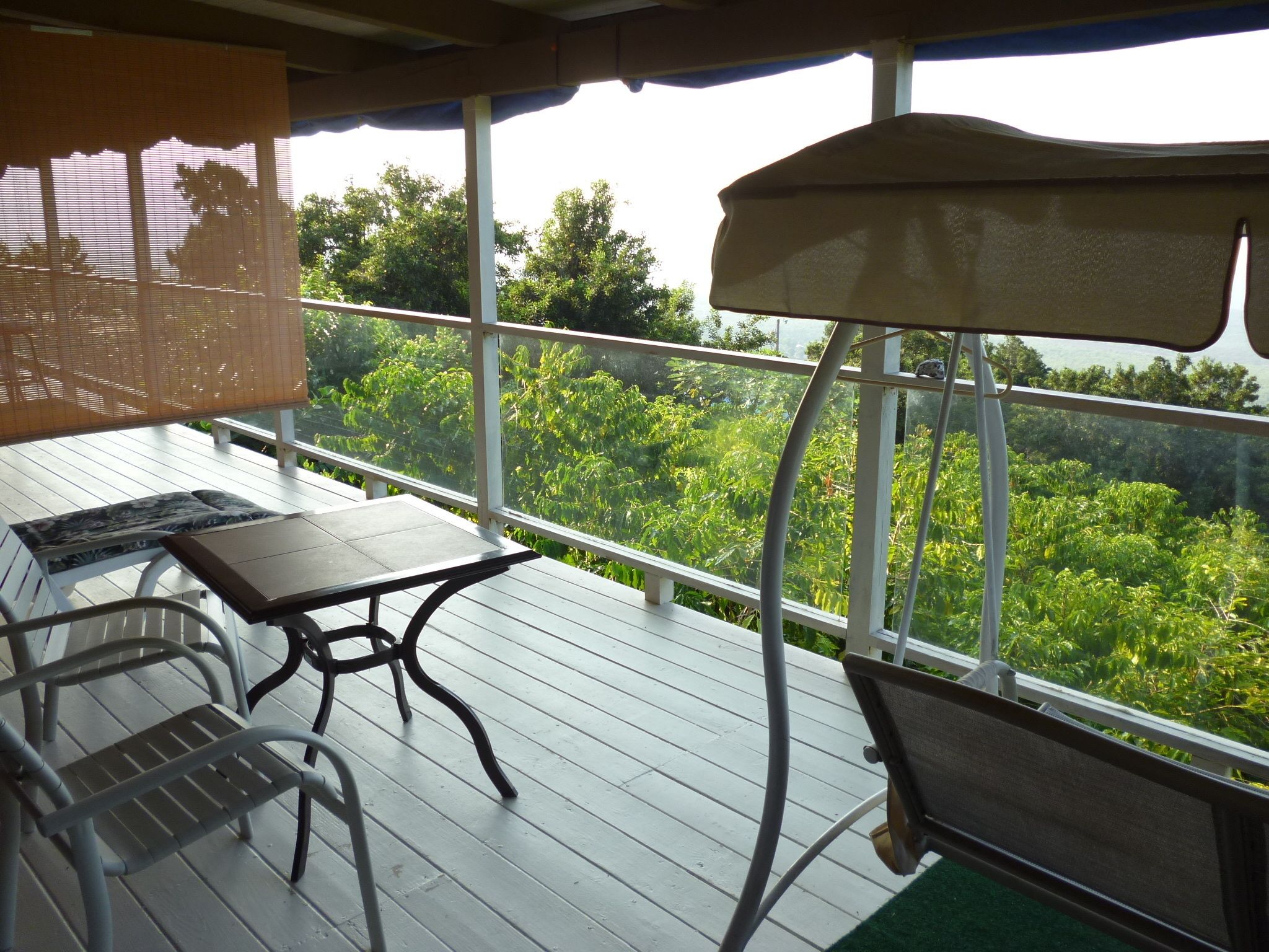 A covered outdoor deck with a table and chairs, overlooking a lush green landscape.