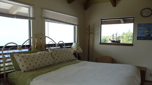 A bedroom with a large bed, two windows with blinds, a wooden floor lamp, a chair, and a painting of a ship on the wall. - A Beautiful Edge of the World B&B (Captain Cook)
