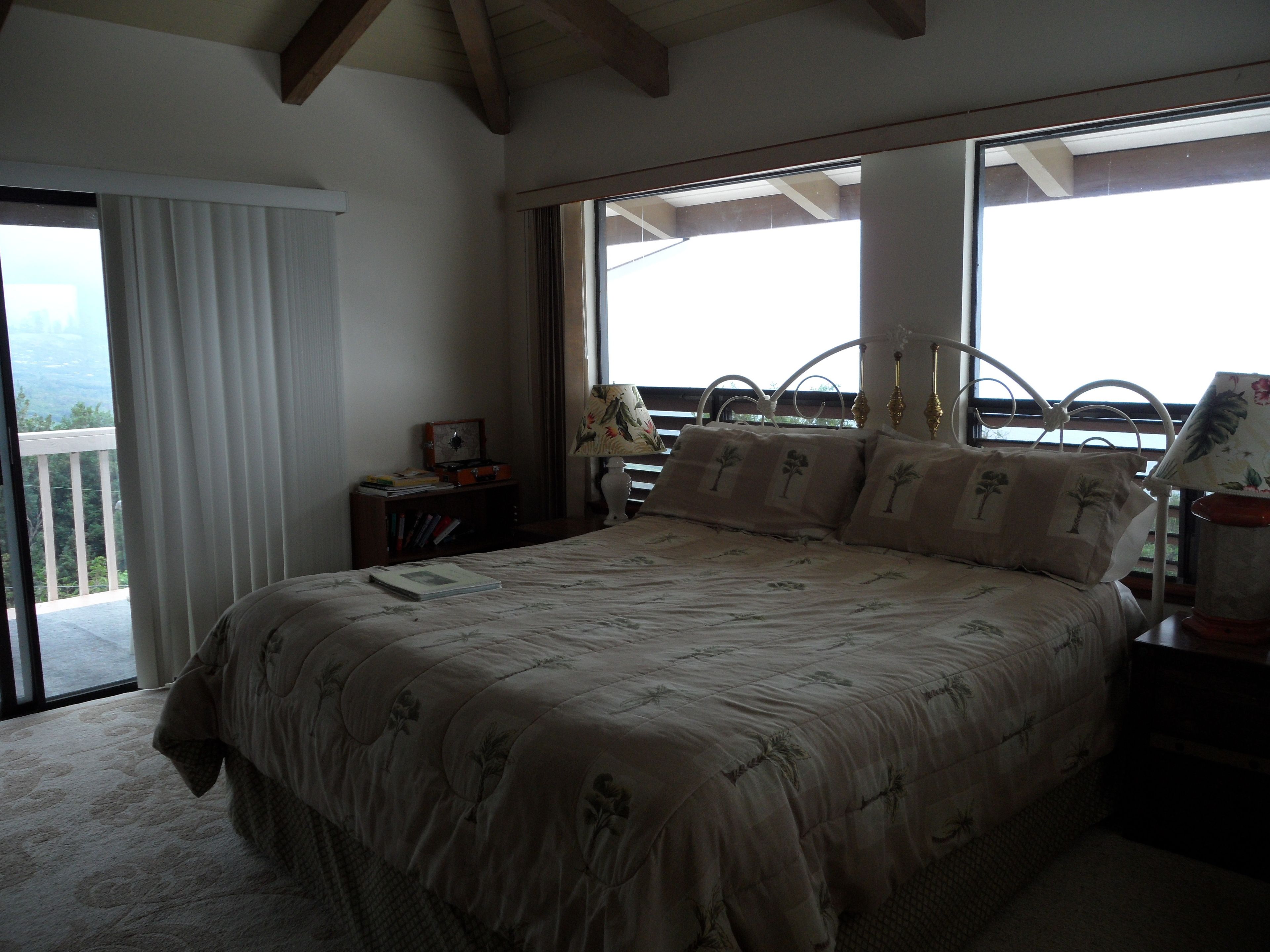 A bedroom with a large bed, a nightstand, a lamp, and a view of the outdoors through a window.