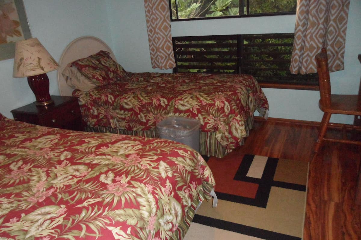 Una habitación con dos camas, una silla de madera, una lámpara y una ventana con cortinas.