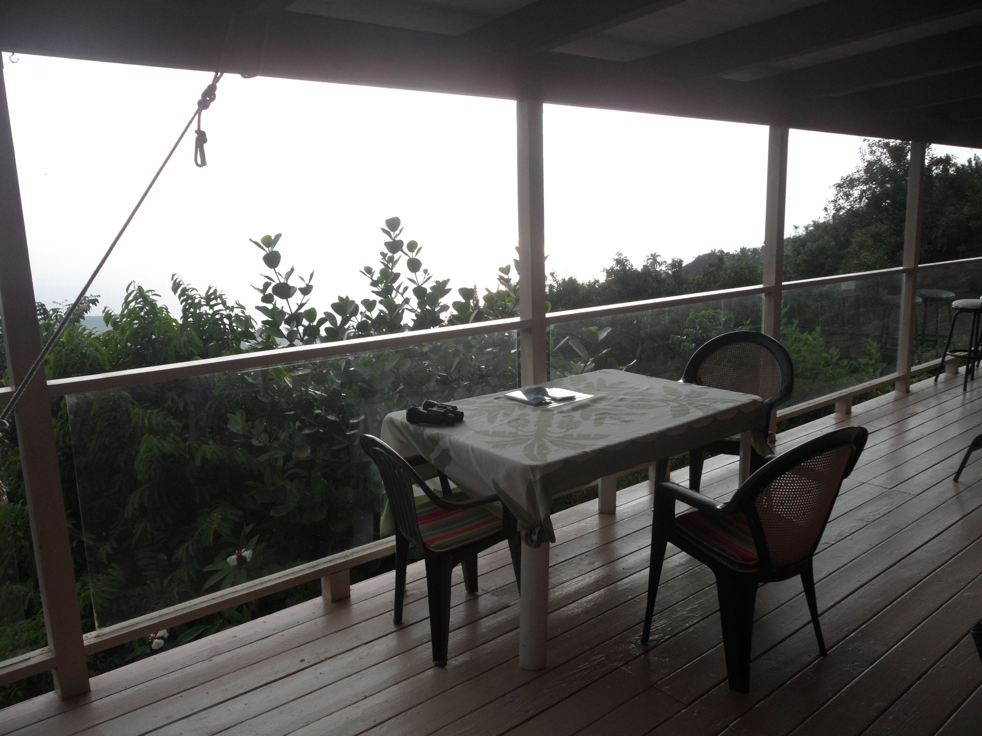 A covered outdoor area with a table and chairs, overlooking a garden.