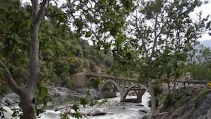A stone bridge over a flowing river, surrounded by trees and rocky terrain. - The Gateway Restaurant & Lodge (Three Rivers)