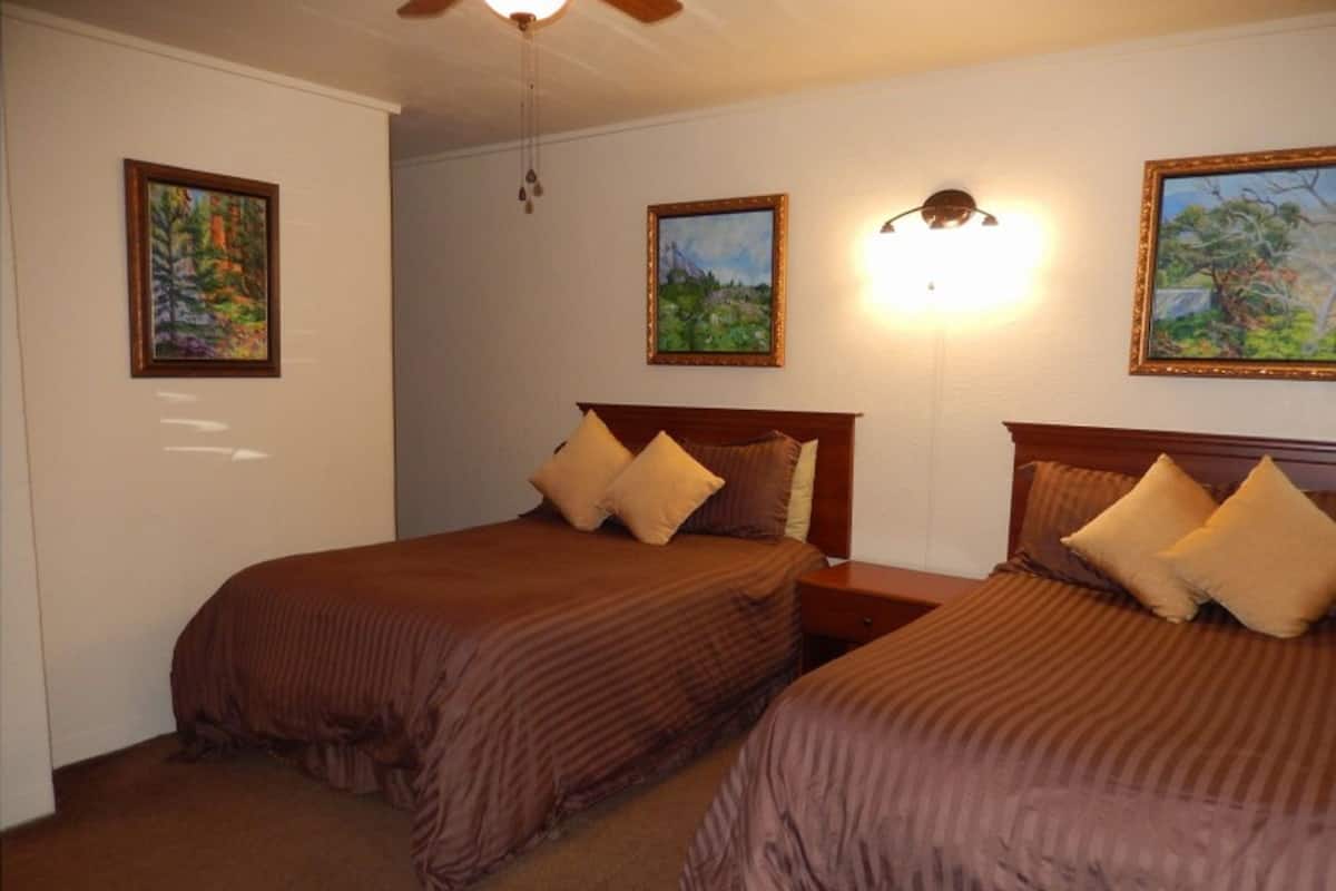 A hotel room with two beds, a ceiling fan, and wall-mounted artwork.