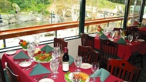 A dining area with tables set for a meal, featuring a view of a natural landscape through large windows. - The Gateway Restaurant & Lodge (Three Rivers)