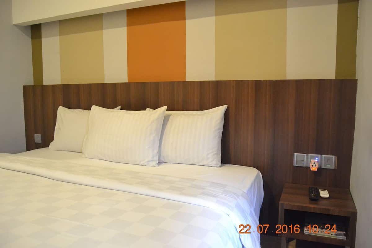 A hotel room with a large bed, a wooden headboard, a nightstand with a phone and a remote control, and a wall with a striped pattern.
