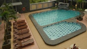 Un área de piscina con dos piscinas, sillas de descanso y plantas en macetas.