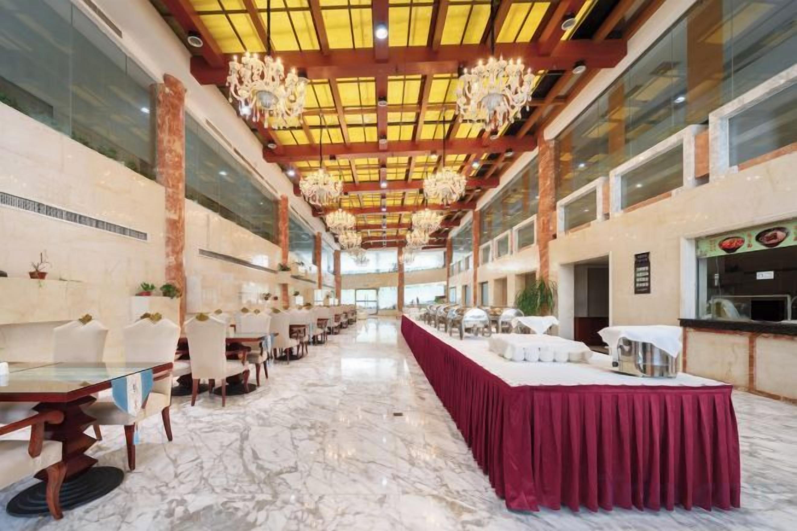 A spacious indoor area with marble flooring, tables, chairs, and a long table draped with a red cloth.