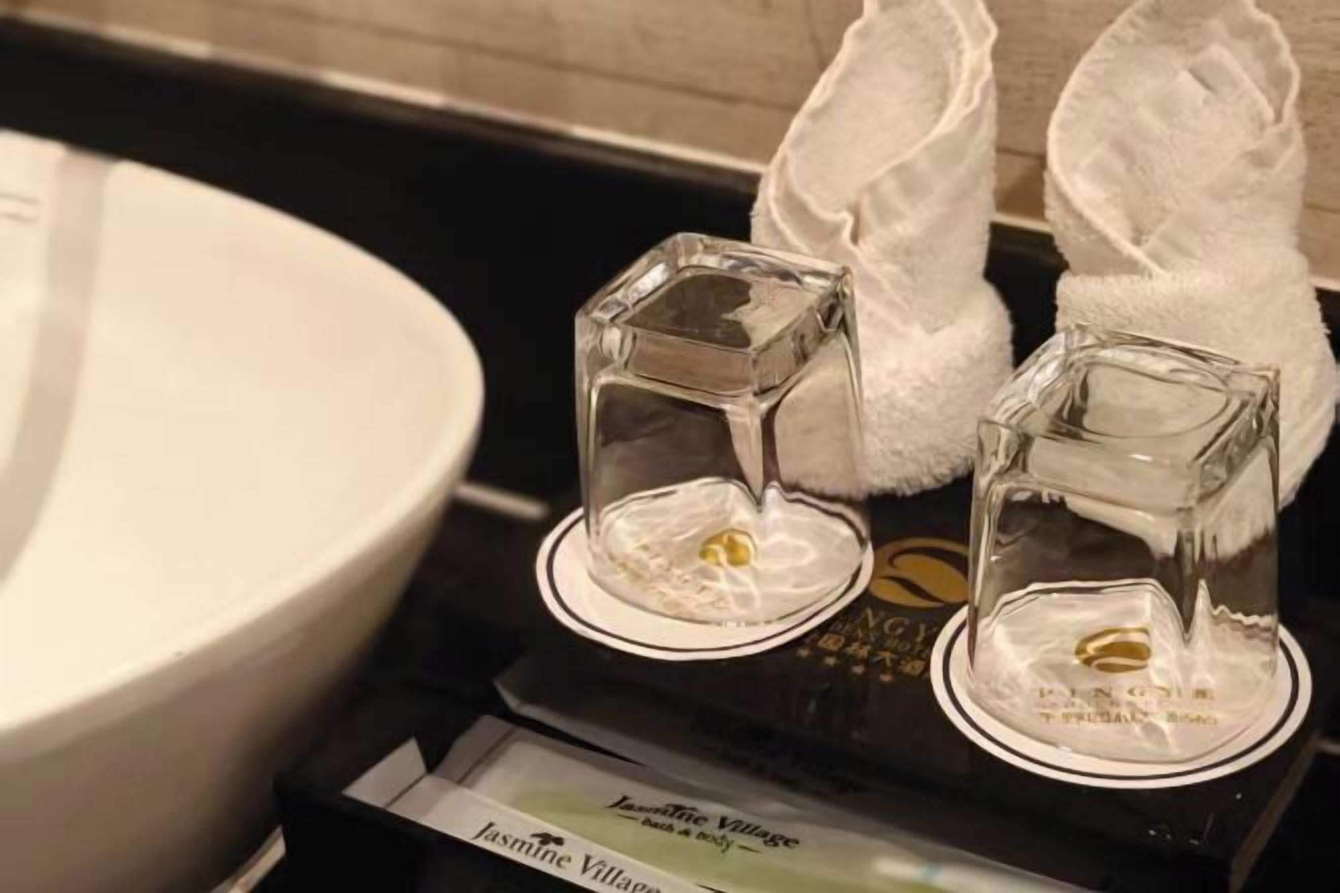 A bathroom with a white sink, two glass containers with white towels, and a sign for Jasmine Village.