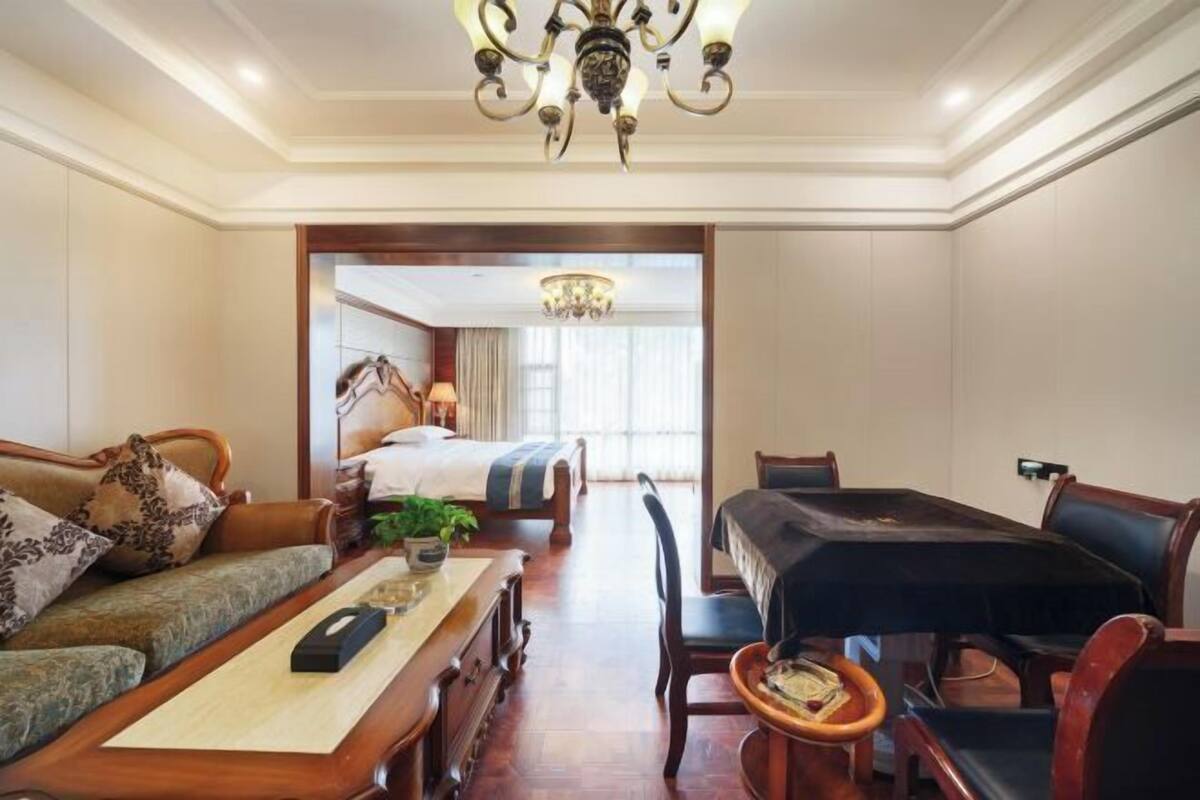 A hotel room with a sofa, a dining table with chairs, a bed, and a chandelier.