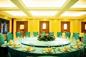 Un salón de conferencias con una mesa redonda, sillas verdes y un centro de mesa con flores.