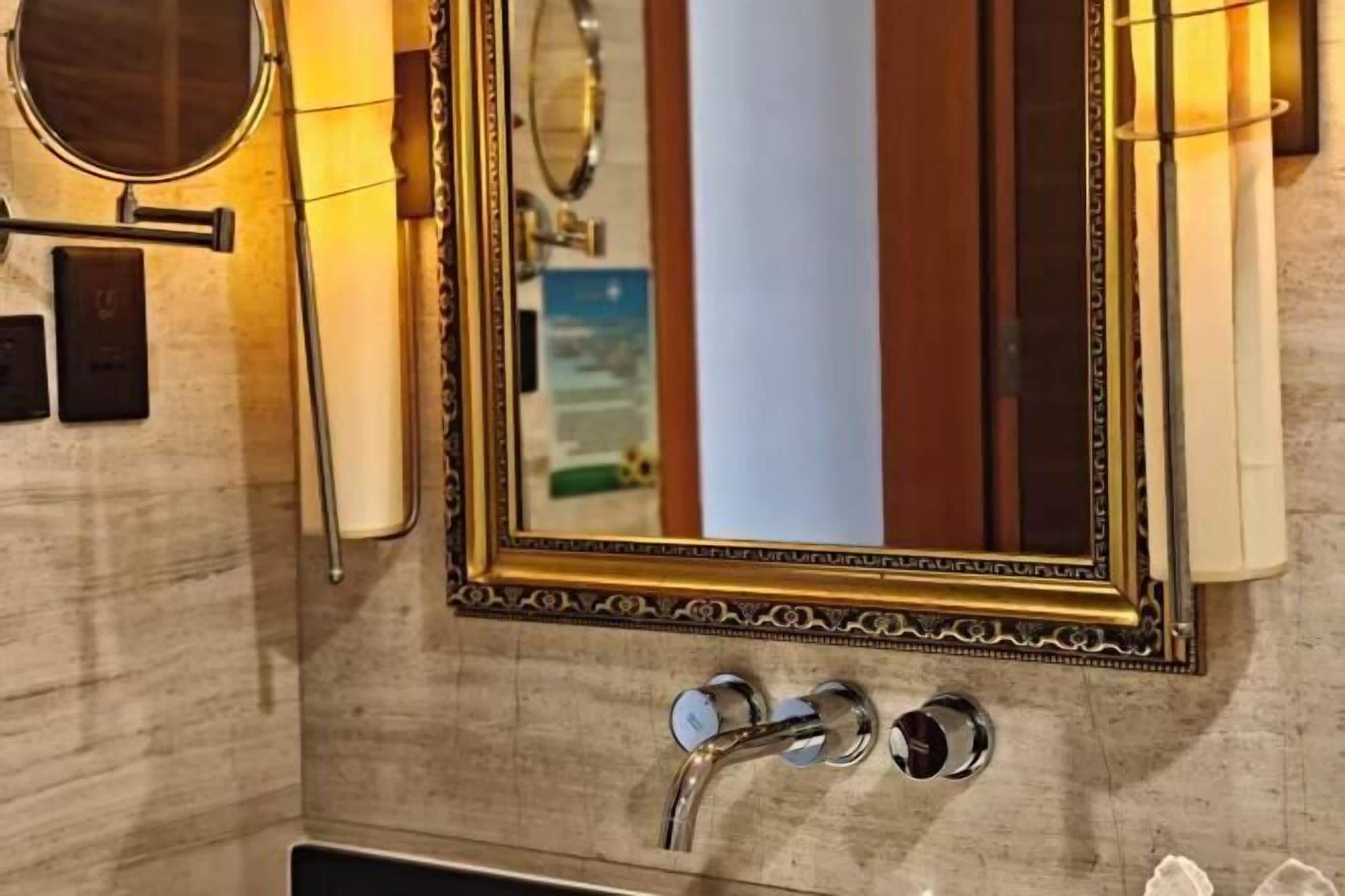 Un meuble-lavabo de salle de bain avec un miroir à cadre doré, un miroir rond et un robinet moderne.