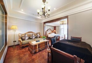 A hotel room with a wooden floor, a sofa with cushions, a desk with a lamp, a bed with a headboard, and a dining table. - Pingye Garden Hotel (Liangping)