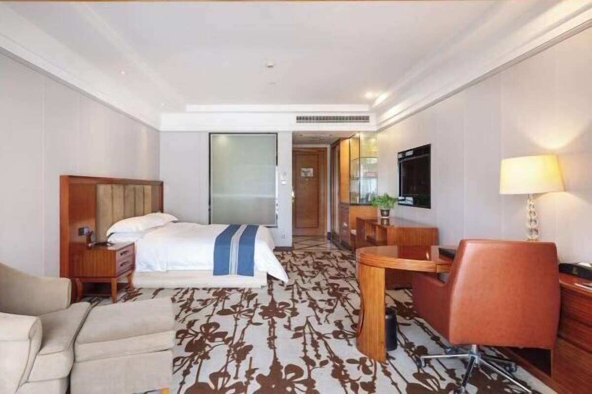 A hotel room with a bed, a desk, a chair, a TV, and a lamp.