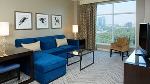 A modern hotel room with a blue sofa, a glass coffee table, a TV, and framed artwork on the wall. - Hyatt Regency Atlanta Perimeter at Villa Christina (Atlanta)