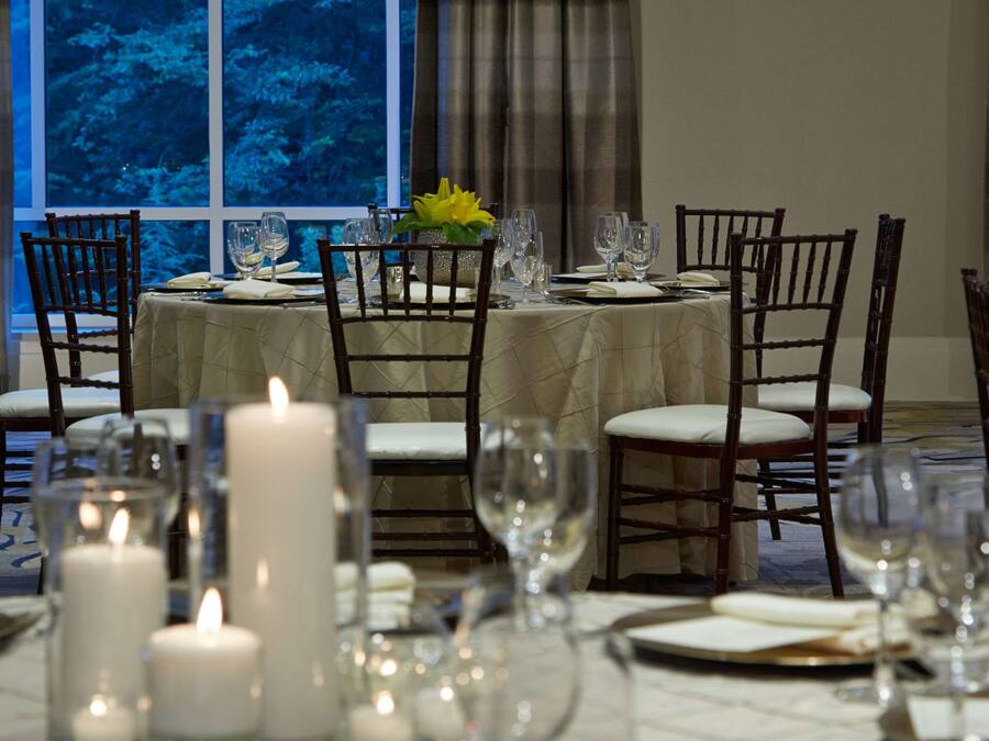 A dining table set for six with chairs, candles, and a window view.