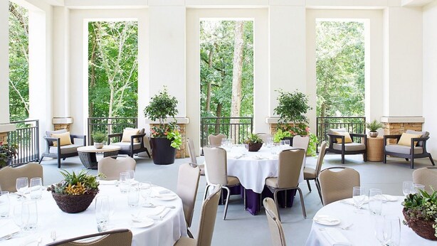 A spacious outdoor dining area with multiple tables and chairs, surrounded by large windows offering views of a lush green forest. - Hyatt Regency Atlanta Perimeter at Villa Christina (Atlanta)