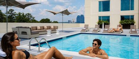 A rooftop pool area with lounge chairs, a seating area, and a view of the city skyline.