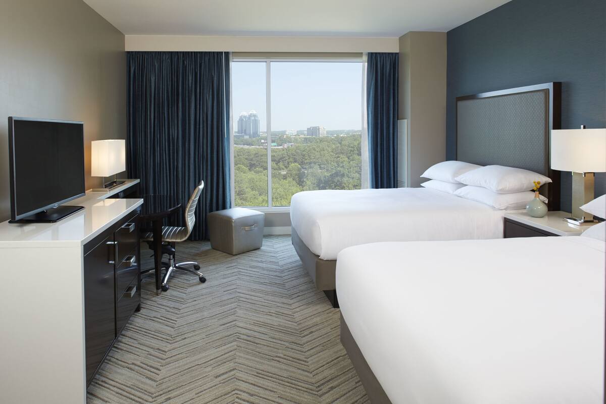 Habitación de hotel con dos camas, un escritorio con ordenador, una silla y televisor.