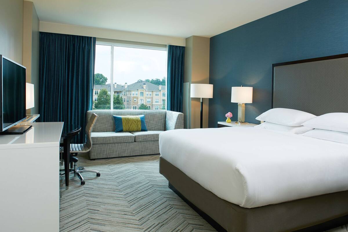 Una habitación de hotel con una cama grande, un sofá, un escritorio y un televisor.