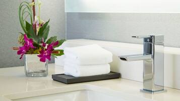 Un baño moderno con un grifo cromado, una bañera blanca y un pequeño jarrón con flores moradas en la encimera.