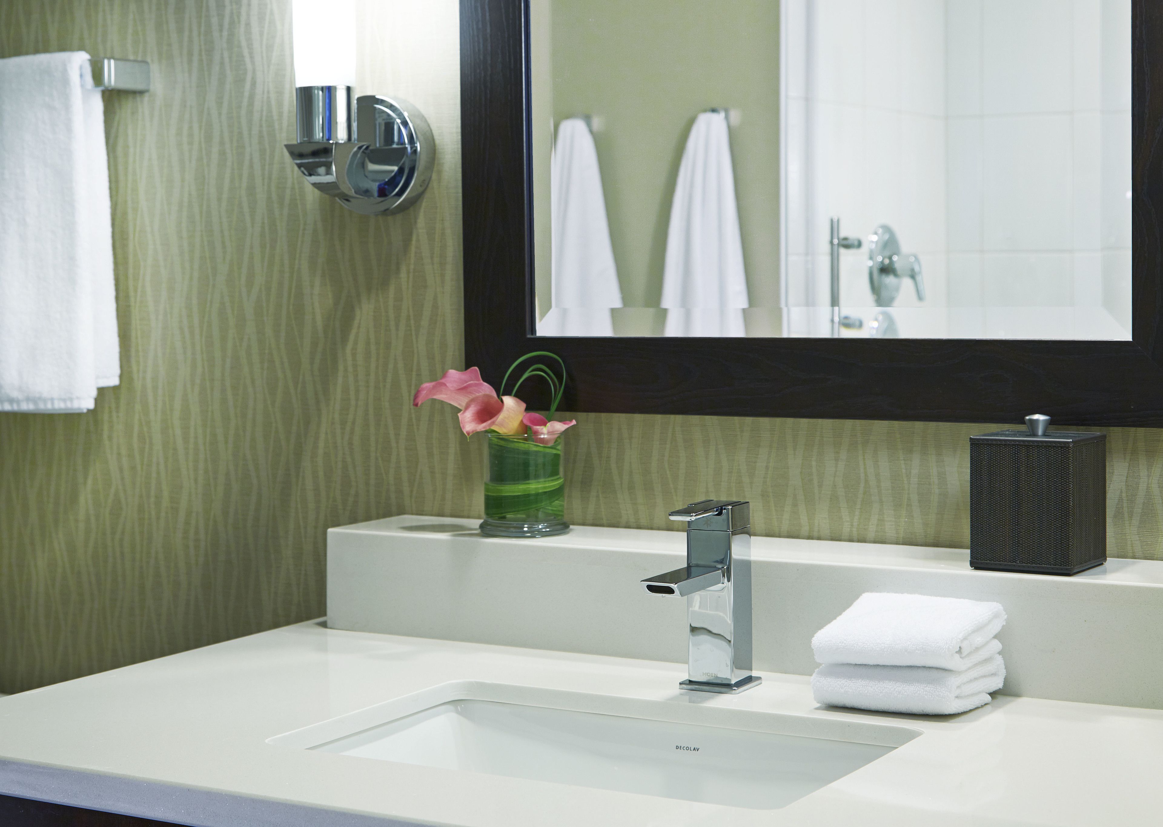 A modern bathroom with a white sink, a mirror, and a vase with flowers.