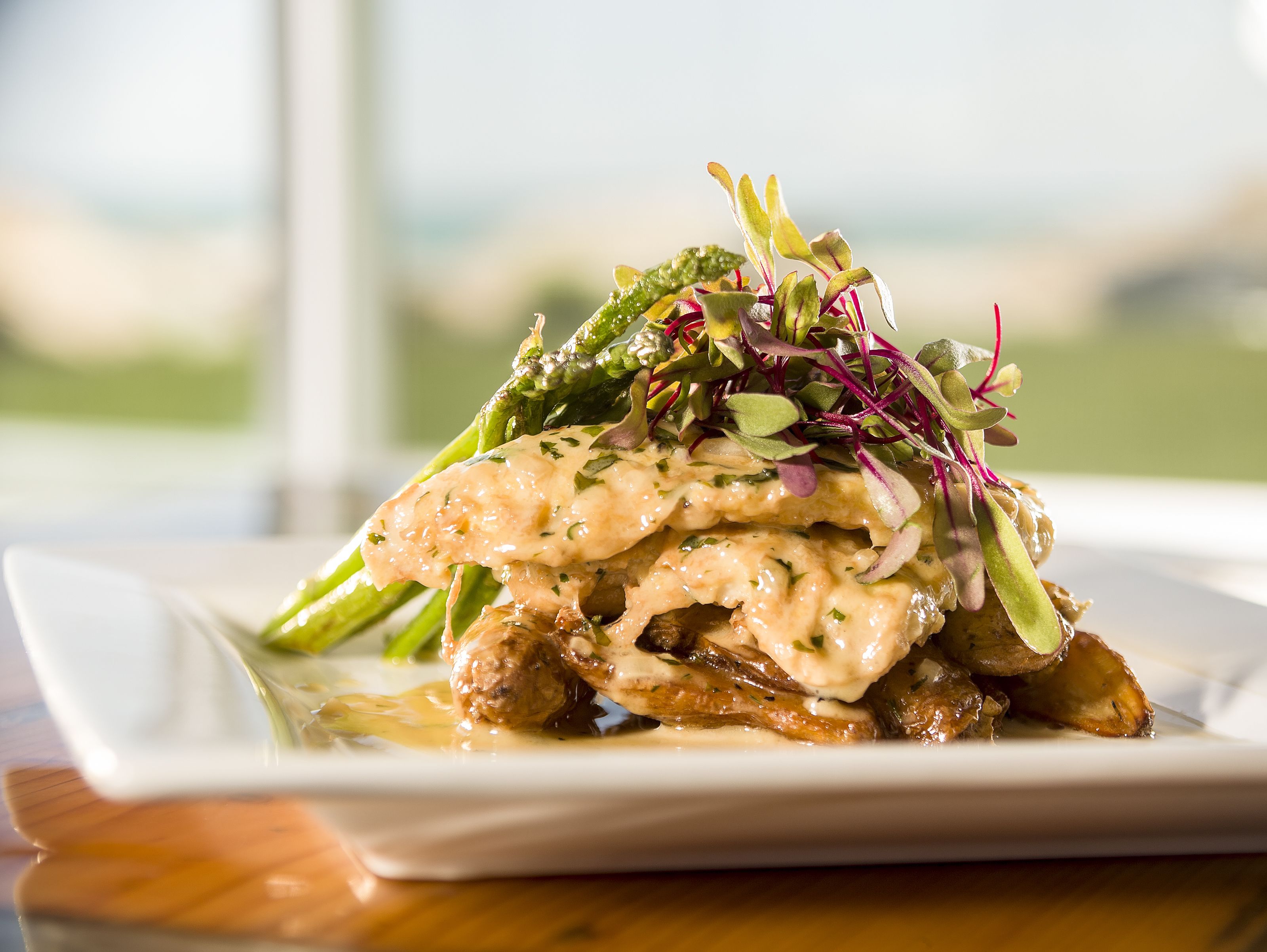 A plate of food with a creamy sauce, asparagus, and greens on a white plate.