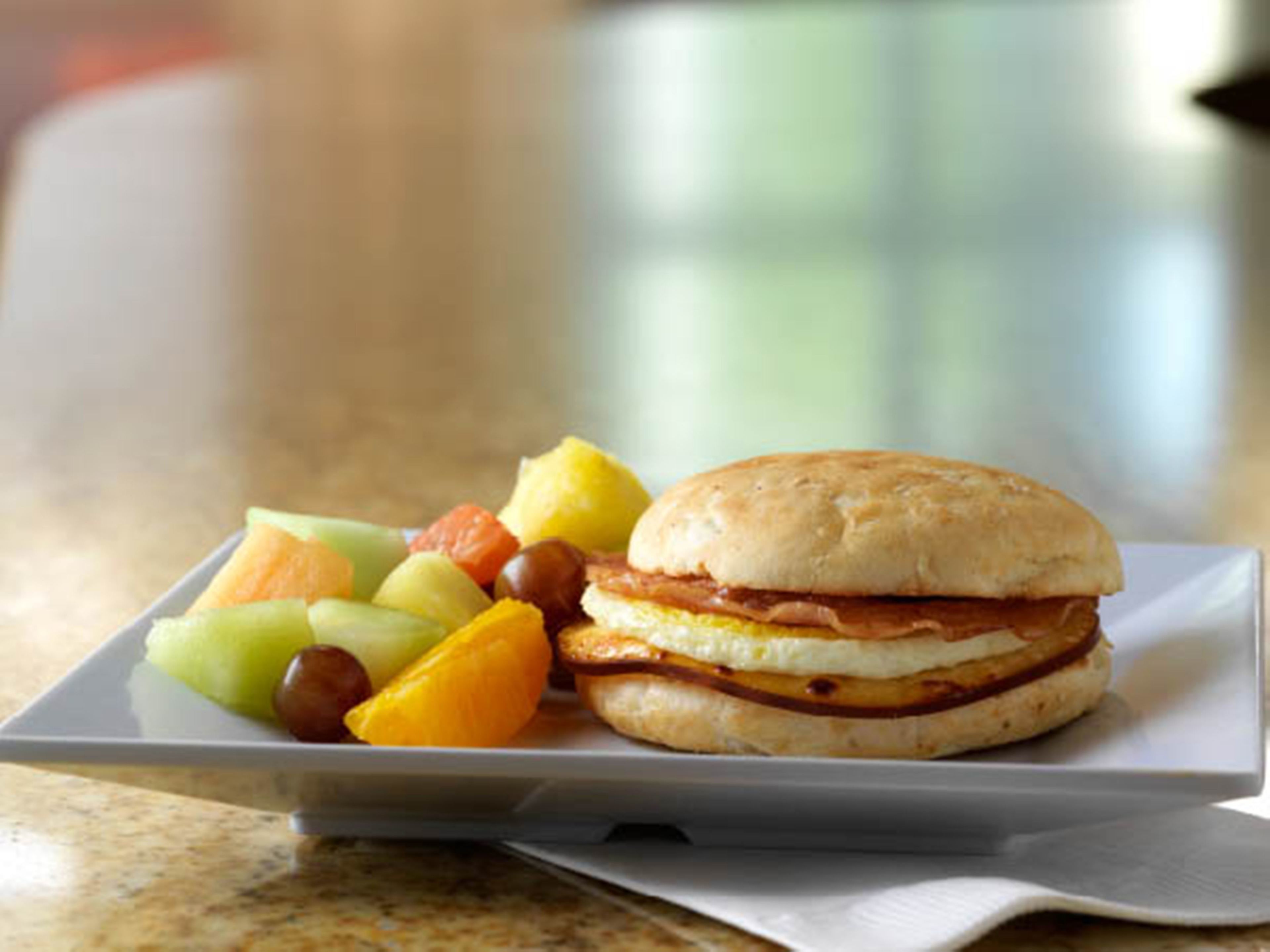 A sandwich with a biscuit on a plate, accompanied by various fruits.