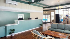 A reception area with a wooden reception desk, a sofa, wicker chairs, and potted plants. - Pleasant View Inn (Westerly)