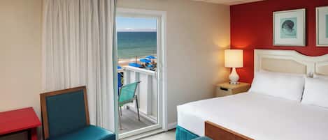Ein Hotelzimmer mit Bett, Stuhl, Tisch und Blick auf den Strand.