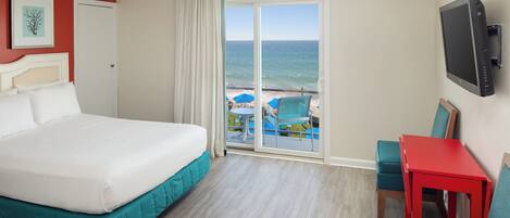 A hotel room with a large bed, a red table, teal chairs, a TV, and a view of the ocean through a sliding glass door.