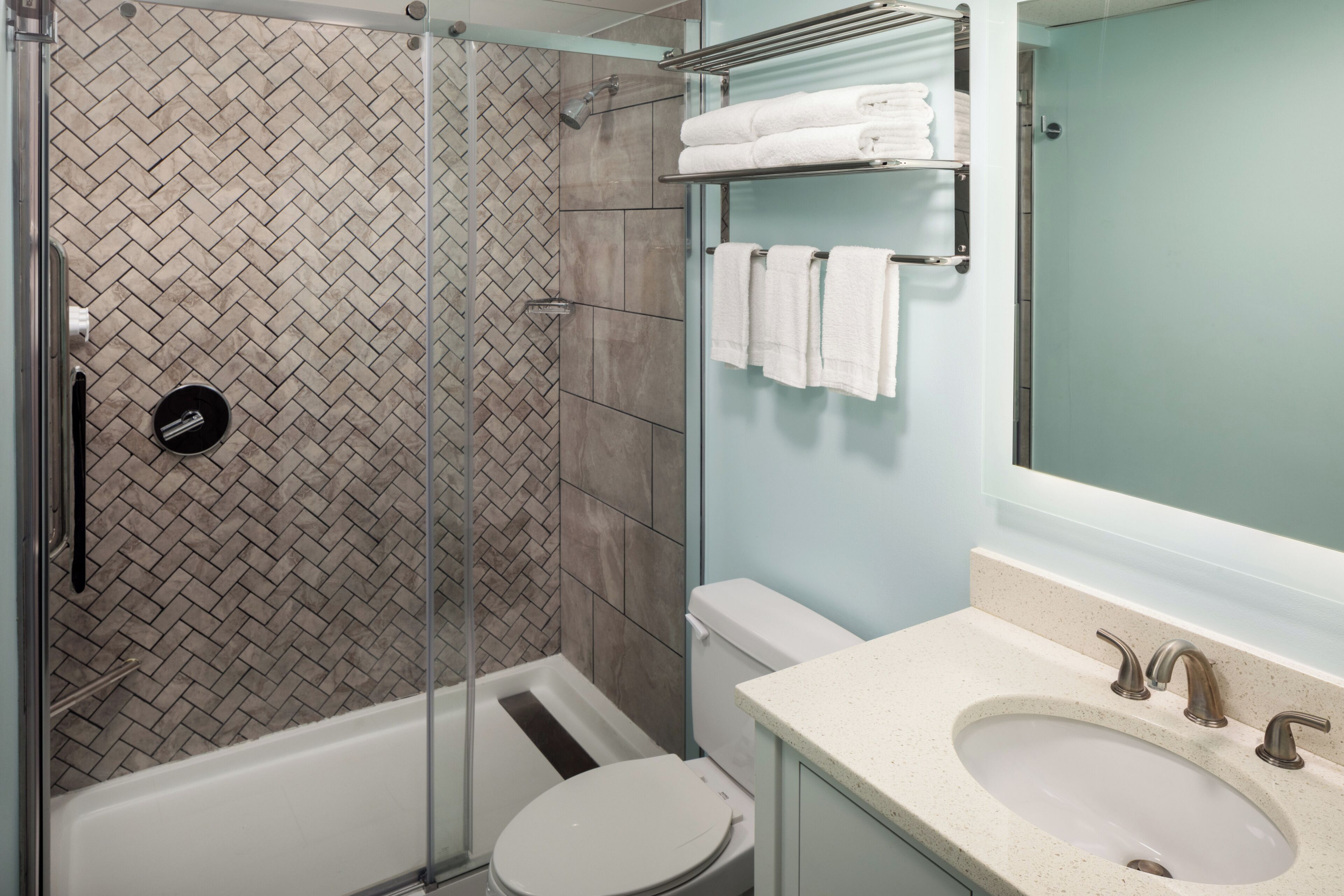 A modern bathroom with a glass-enclosed shower, a white toilet, a sink with a mirror, and a towel rack with folded towels.
