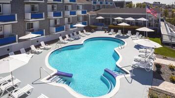A swimming pool with lounge chairs and umbrellas, surrounded by a building with balconies.
