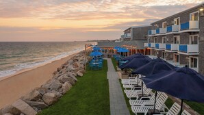 A beachfront hotel with outdoor seating and umbrellas, a stone wall, and a view of the ocean. - Pleasant View Inn (Westerly)