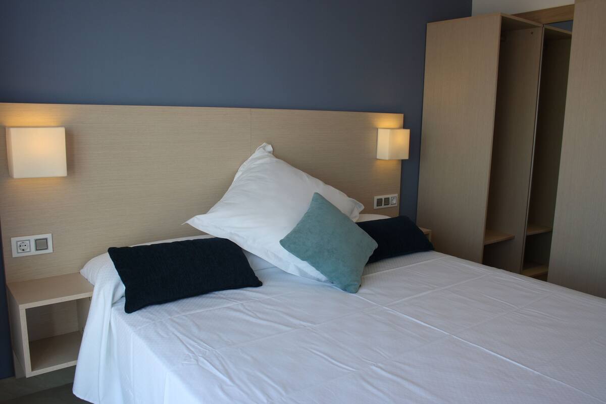 A neatly made bed with white bedding and two pillows, a bedside table with a lamp, and a wardrobe with sliding doors.