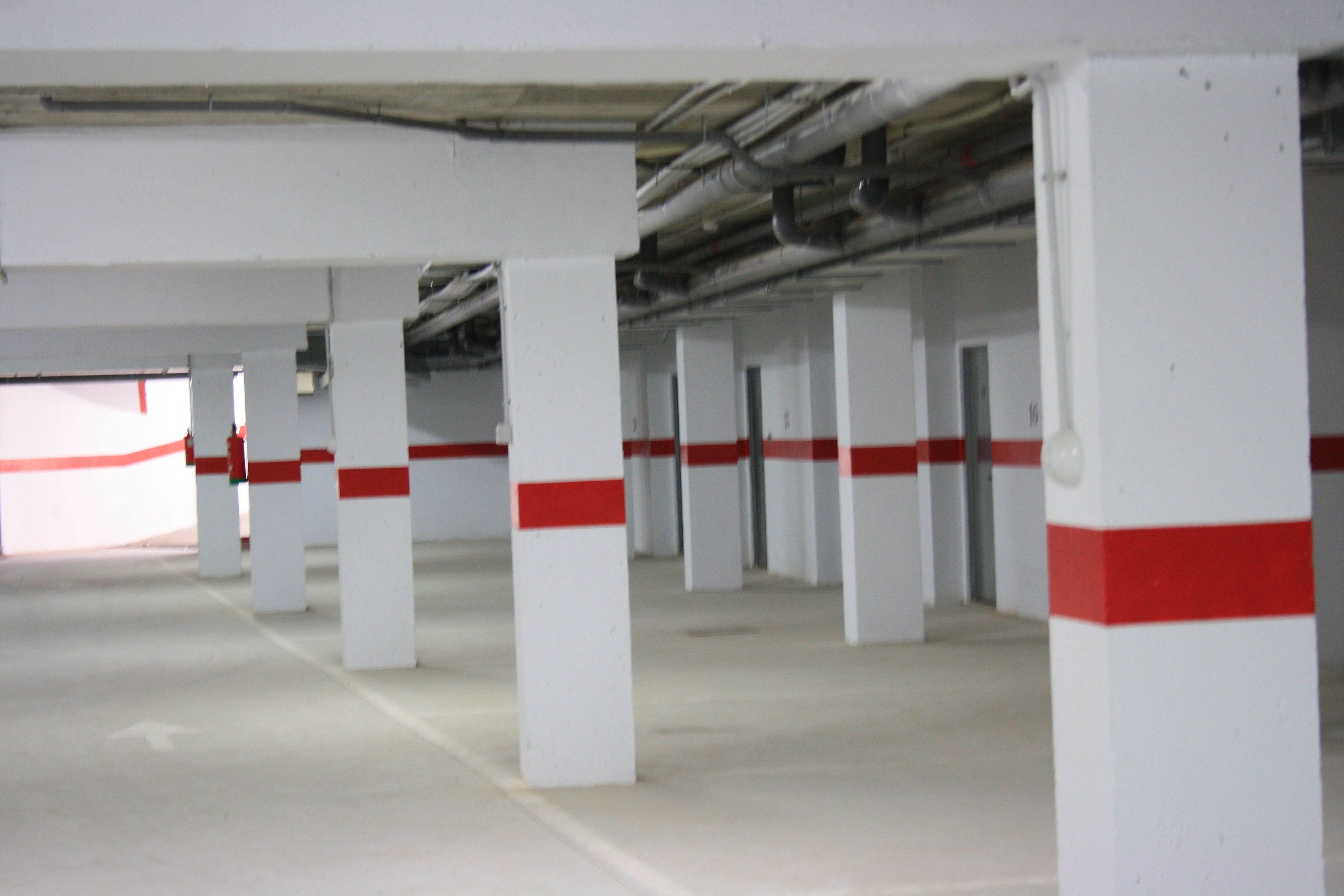 An indoor parking garage with white pillars and red stripes.