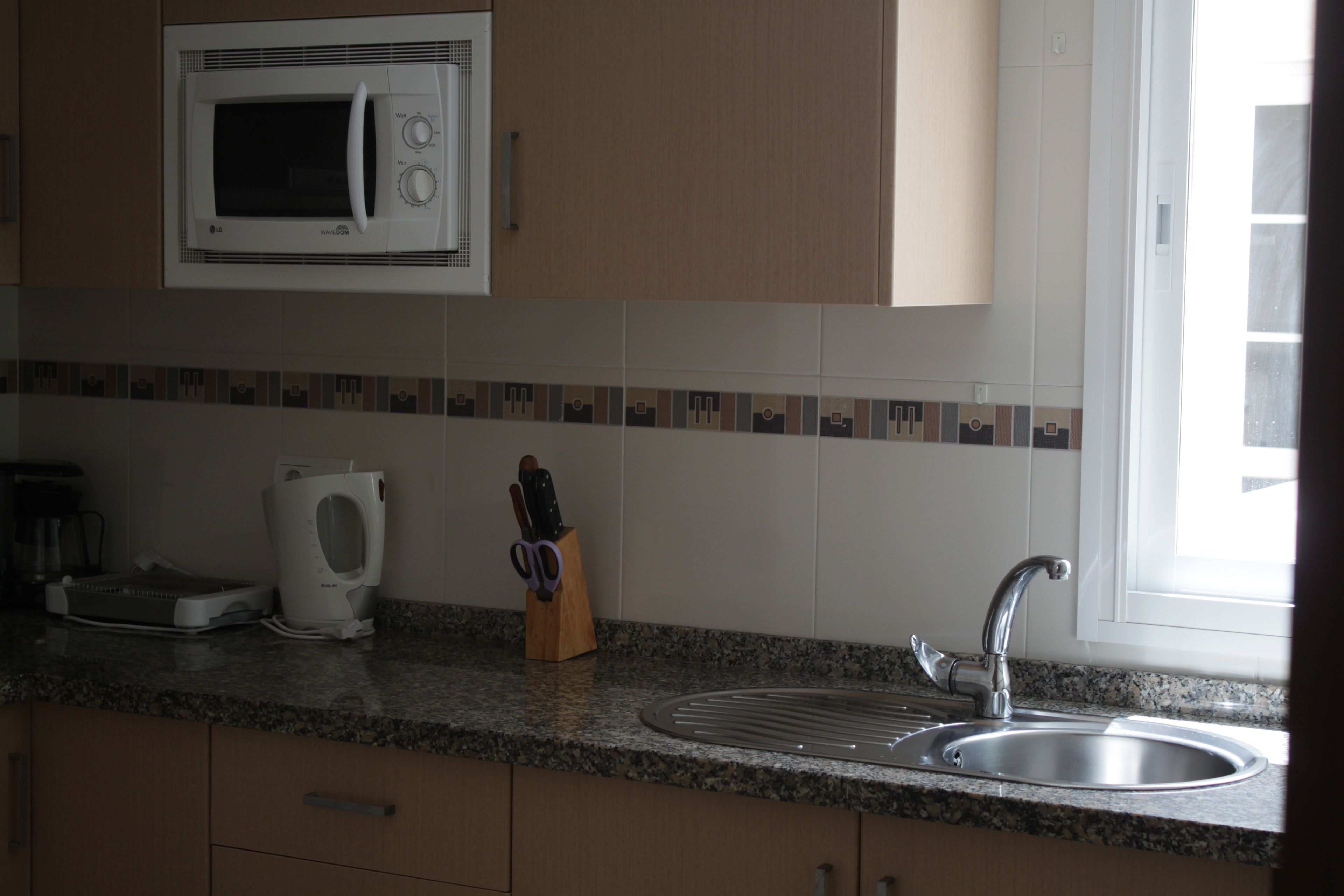 A kitchen with a microwave, toaster, sink, and knife block.