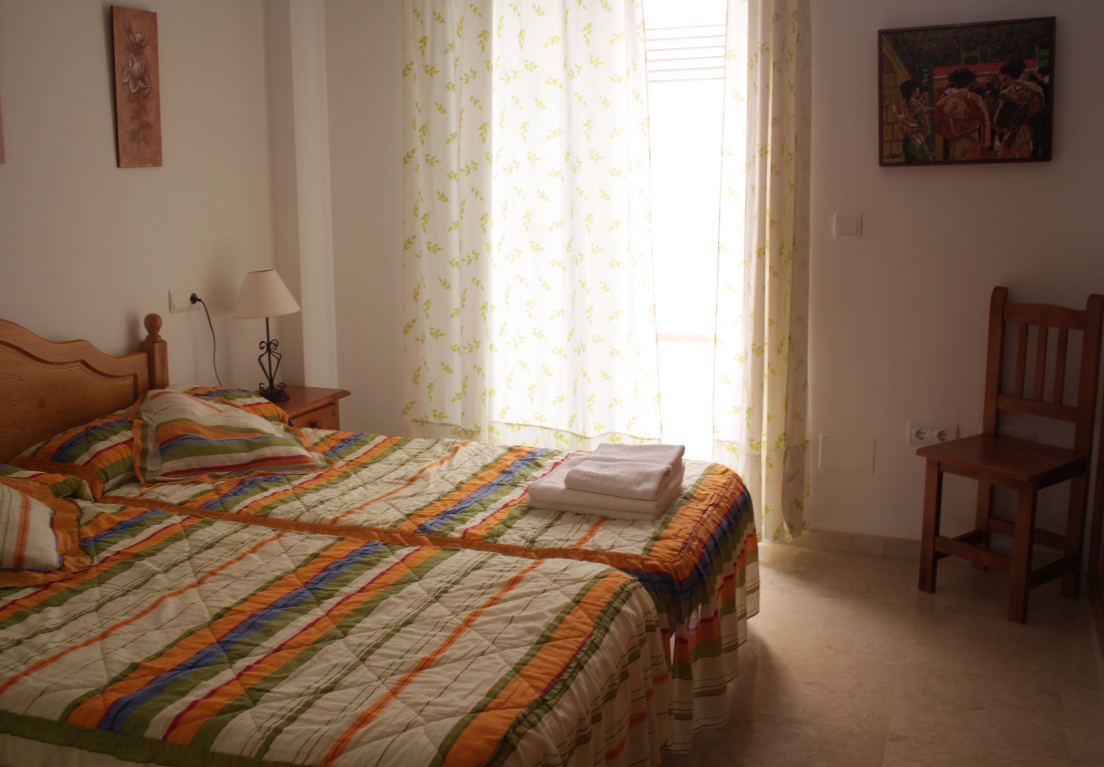 Un dormitorio con dos camas, una silla, una lámpara y un cuadro en la pared.