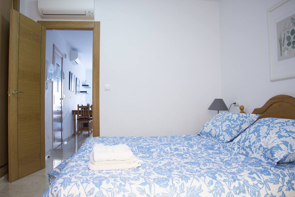 A bedroom with a bed, a bedside lamp, and a door leading to another room.
