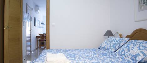 Un dormitorio con cama, lámpara de noche y puerta que da a otra habitación.
