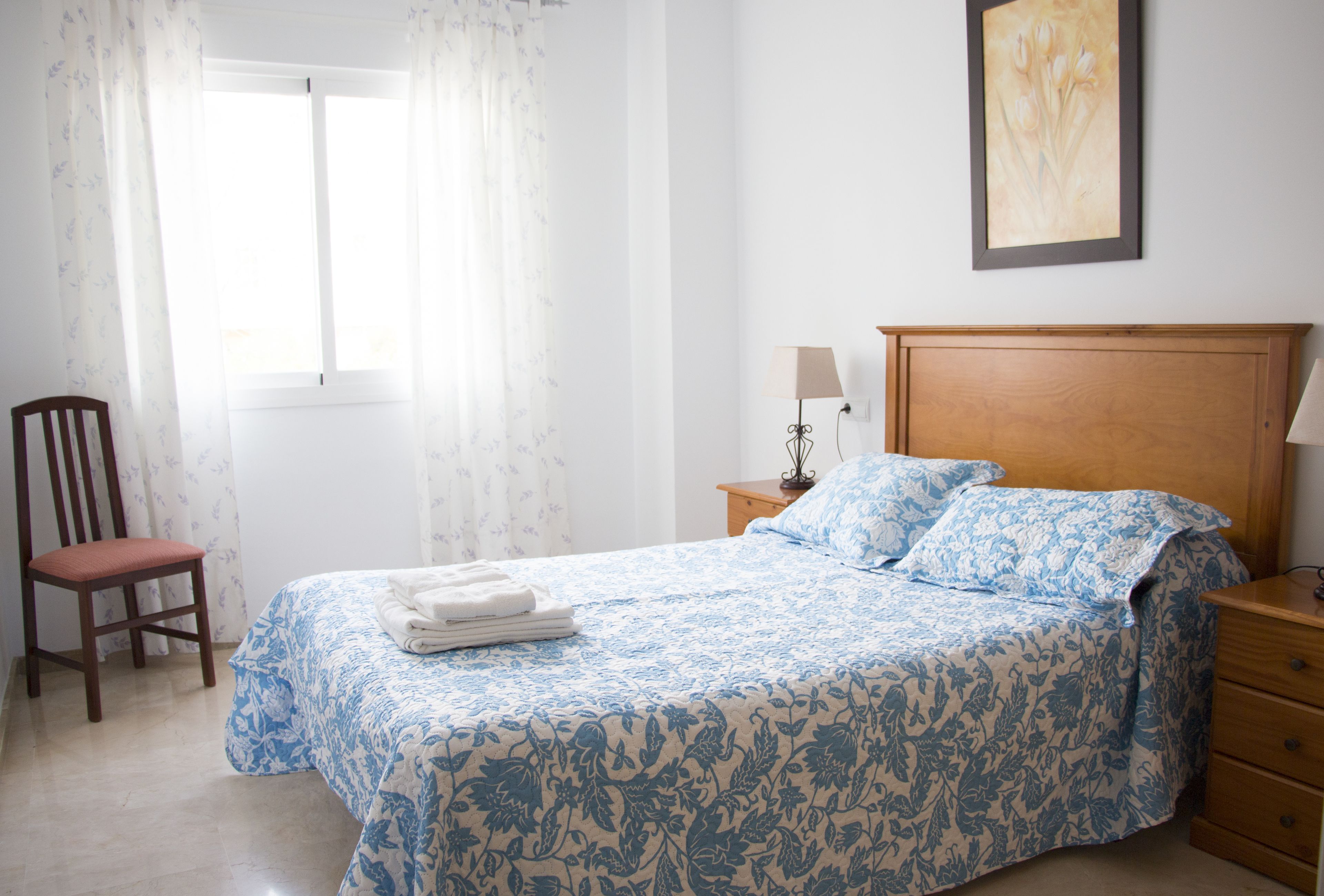 Une chambre à coucher avec un lit, une chaise, une table de chevet et un tableau au mur.