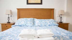 Un letto rifatto con cura, con una coperta a motivi floreali e due cuscini, affiancato da comodini con lampade e un quadro incorniciato sopra il letto.