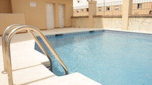 Una piscina con una scala in metallo, pareti color crema e una facciata in pietra.
