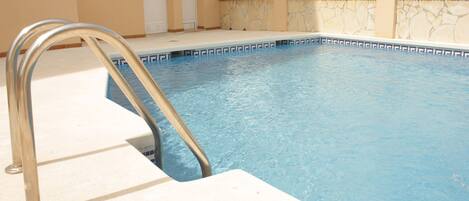 En swimmingpool med en metalstige, beige vægge og en stenvæg.